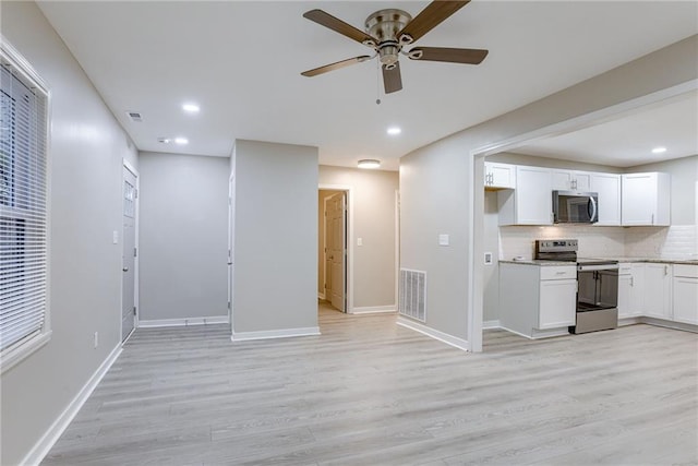 kitchen featuring decorative backsplash, white cabinets, light wood-type flooring, and appliances with stainless steel finishes