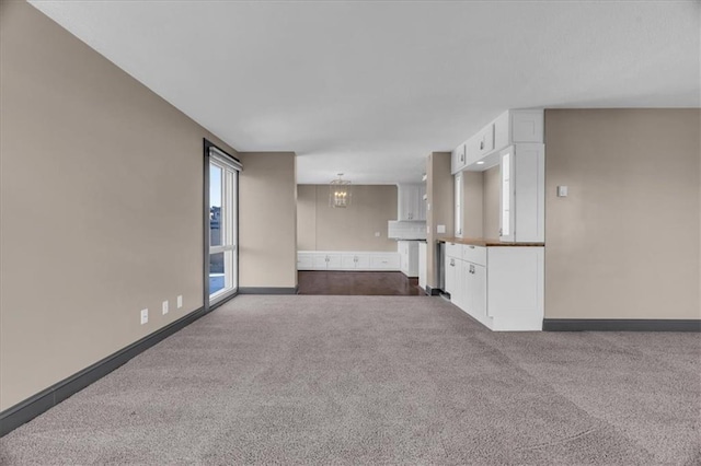 unfurnished living room with baseboards, dark colored carpet, and a chandelier