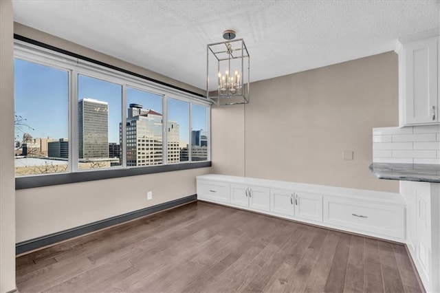 unfurnished dining area with dark wood-style floors, a city view, a notable chandelier, and a textured ceiling