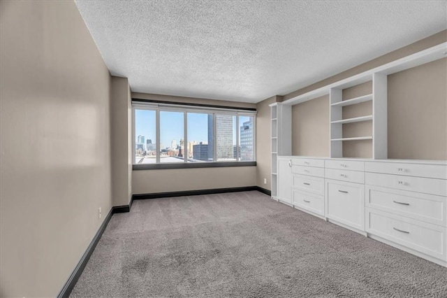 unfurnished bedroom featuring a view of city, a textured ceiling, baseboards, and light colored carpet