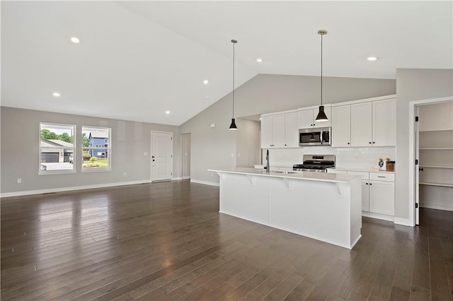 kitchen featuring appliances with stainless steel finishes, decorative light fixtures, white cabinetry, and an island with sink