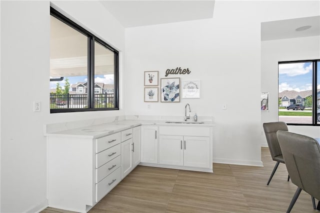 bar with white cabinets, light stone countertops, and sink