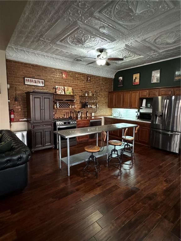 interior space featuring ceiling fan, dark hardwood / wood-style flooring, stainless steel appliances, and brick wall