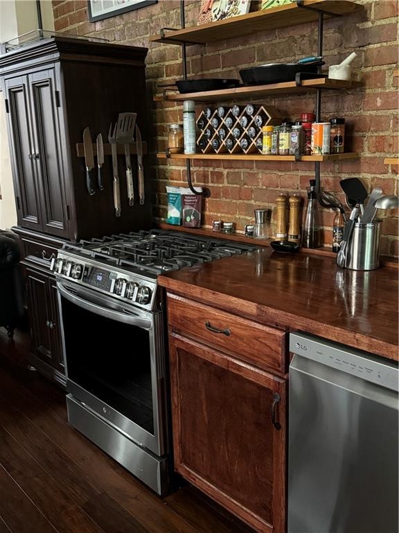 kitchen featuring butcher block counters, appliances with stainless steel finishes, dark wood-type flooring, and brick wall