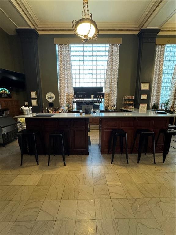 kitchen with a center island, a kitchen bar, ornate columns, and crown molding