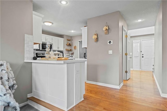 kitchen featuring white cabinets, kitchen peninsula, appliances with stainless steel finishes, and light hardwood / wood-style flooring