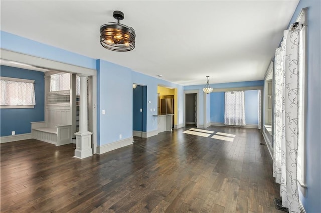 unfurnished living room with decorative columns and dark wood-type flooring