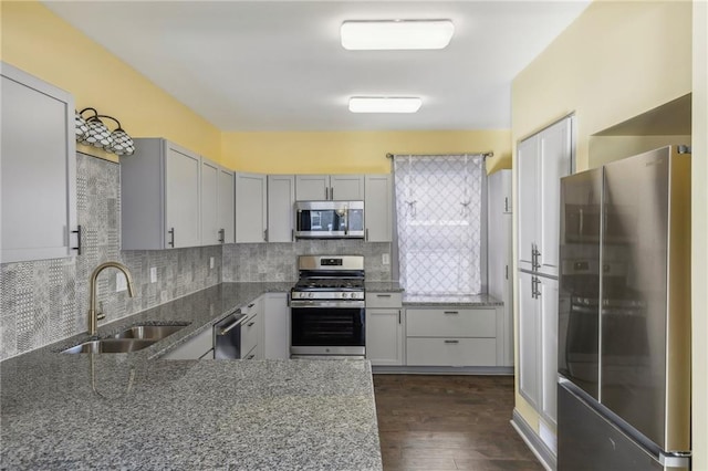 kitchen featuring appliances with stainless steel finishes, dark hardwood / wood-style flooring, dark stone countertops, sink, and backsplash