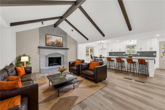 living room featuring a fireplace, vaulted ceiling with beams, and light hardwood / wood-style flooring