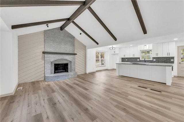 unfurnished living room with a brick fireplace, lofted ceiling with beams, light hardwood / wood-style flooring, and plenty of natural light