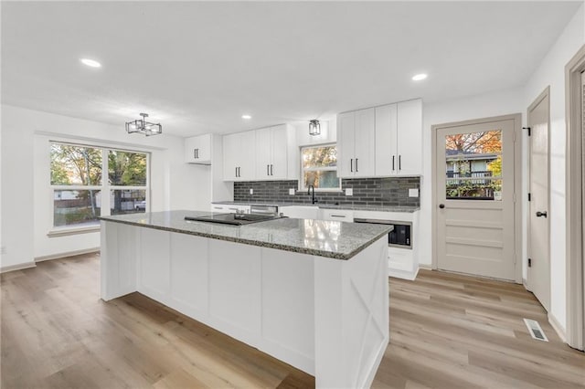 kitchen with a center island, dark stone countertops, white cabinetry, and light wood-type flooring