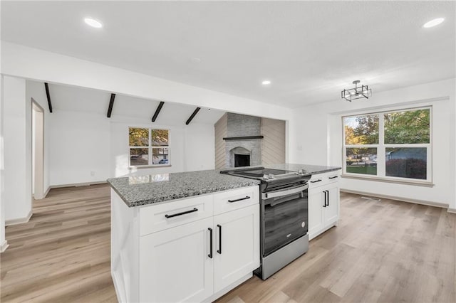 kitchen with stainless steel range with electric cooktop, dark stone counters, white cabinets, light hardwood / wood-style flooring, and a fireplace