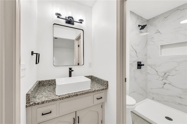 bathroom featuring a tile shower, vanity, and toilet