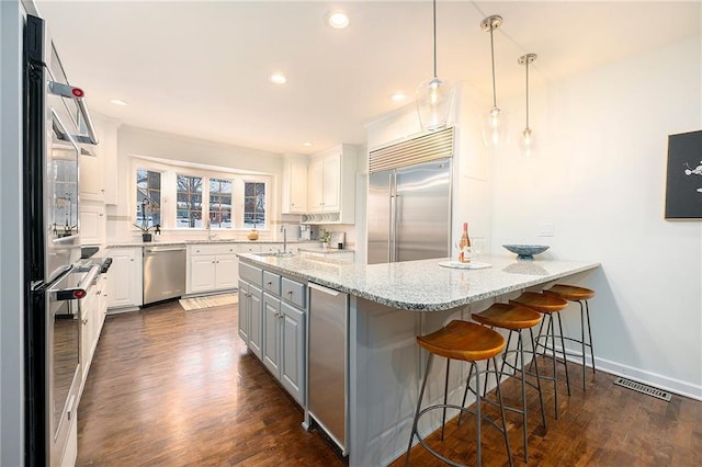 kitchen featuring stainless steel appliances, white cabinetry, hanging light fixtures, and light stone counters