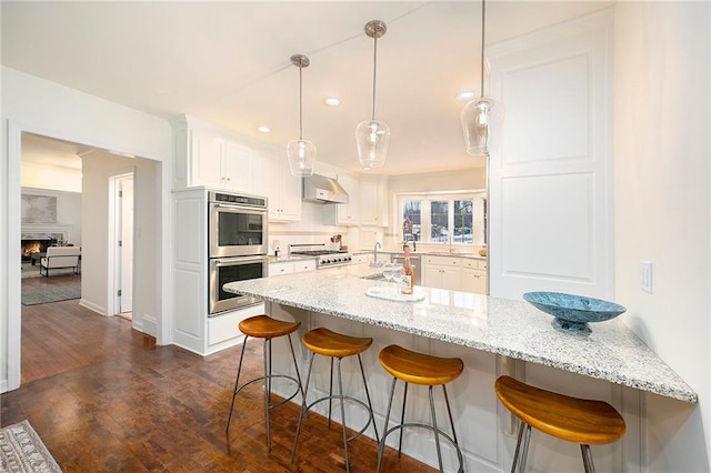 kitchen with appliances with stainless steel finishes, light stone counters, extractor fan, white cabinetry, and hanging light fixtures