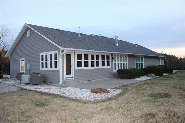 back house at dusk with a yard, a patio area, and central air condition unit