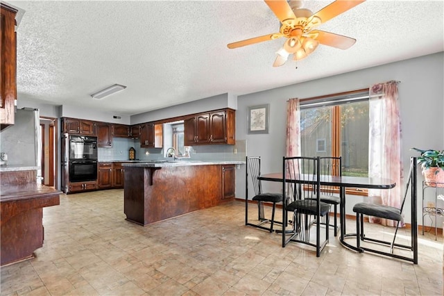 kitchen featuring kitchen peninsula, a breakfast bar, black double oven, ceiling fan, and sink