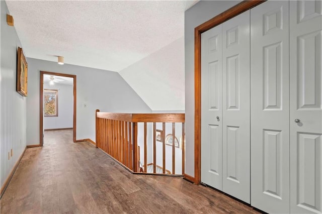 corridor with a textured ceiling, hardwood / wood-style floors, and lofted ceiling