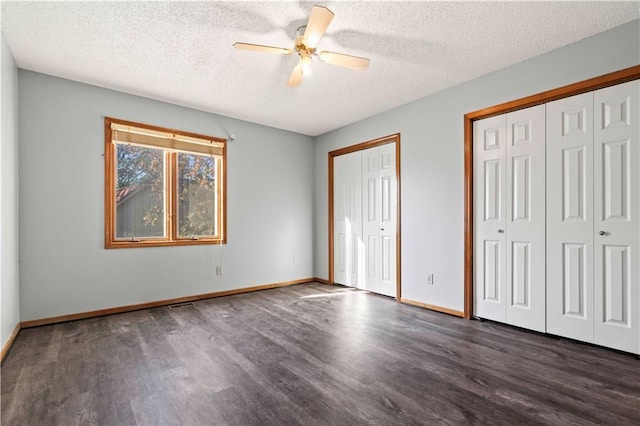 unfurnished bedroom featuring a textured ceiling, two closets, ceiling fan, and dark wood-type flooring