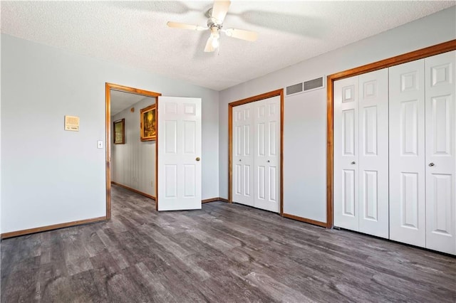 unfurnished bedroom featuring ceiling fan, dark hardwood / wood-style floors, a textured ceiling, and two closets