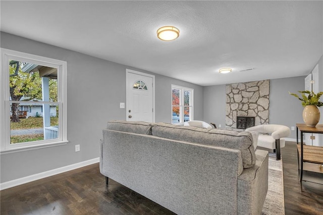 living room featuring a textured ceiling, a stone fireplace, and dark wood-type flooring