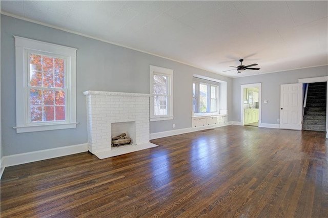 unfurnished living room with ornamental molding, a brick fireplace, ceiling fan, and dark wood-type flooring