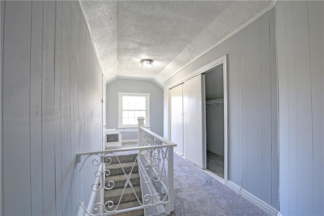 hall featuring carpet flooring, wooden walls, and lofted ceiling