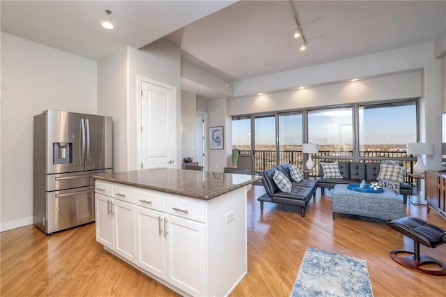 kitchen featuring stainless steel fridge, light wood-type flooring, dark stone counters, a center island, and white cabinetry