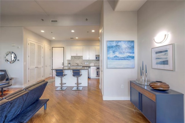 kitchen featuring a kitchen island, light hardwood / wood-style flooring, backsplash, a breakfast bar, and white cabinets