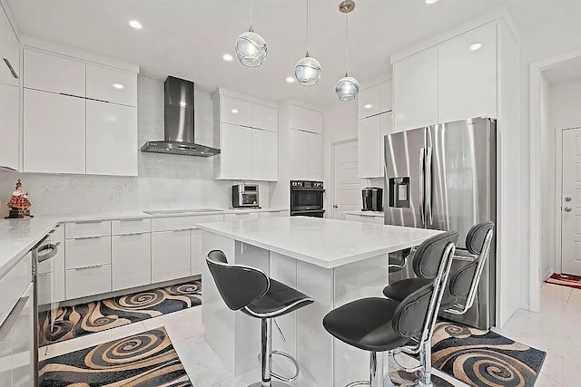 kitchen featuring white cabinets, appliances with stainless steel finishes, a center island, and wall chimney range hood