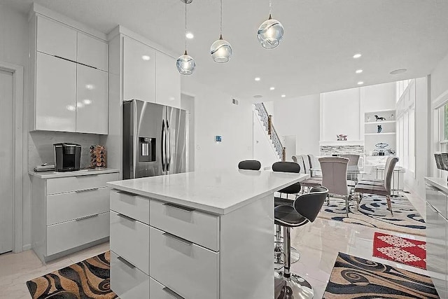 kitchen featuring white cabinets, a kitchen breakfast bar, stainless steel refrigerator with ice dispenser, hanging light fixtures, and a kitchen island