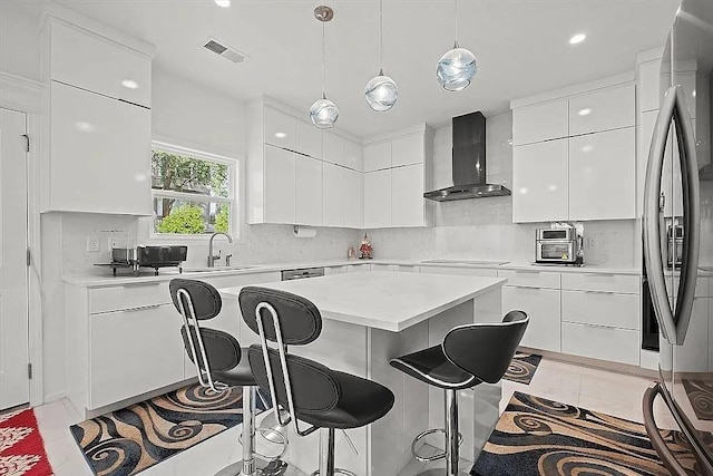 kitchen featuring wall chimney exhaust hood, stainless steel appliances, light tile patterned floors, white cabinetry, and a kitchen island