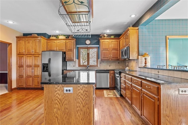 kitchen featuring sink, stainless steel appliances, light hardwood / wood-style flooring, dark stone countertops, and a kitchen island