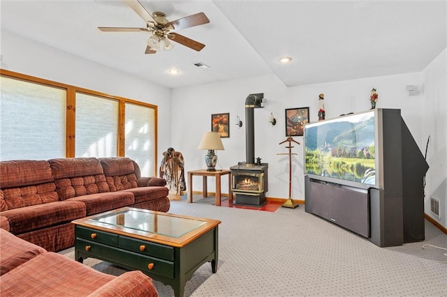 carpeted living room featuring a wood stove and ceiling fan