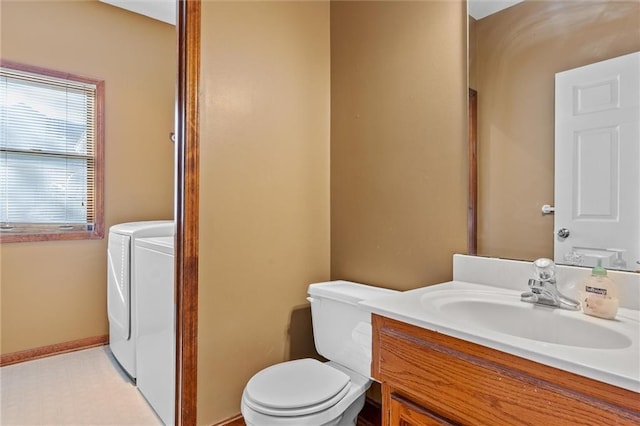 bathroom featuring baseboards, toilet, washer and clothes dryer, and vanity