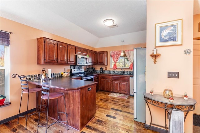 kitchen featuring a peninsula, dark countertops, light wood-style flooring, and appliances with stainless steel finishes