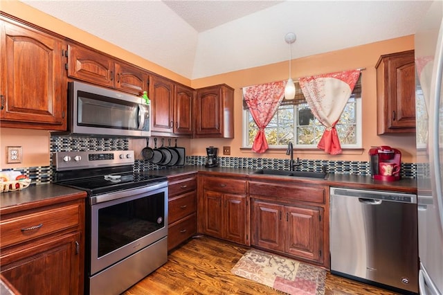 kitchen with dark countertops, dark wood-style flooring, stainless steel appliances, and a sink