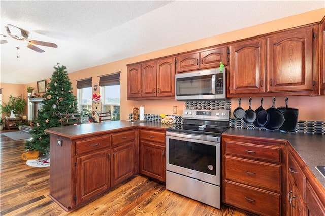 kitchen with ceiling fan, stainless steel appliances, a peninsula, light wood finished floors, and dark countertops