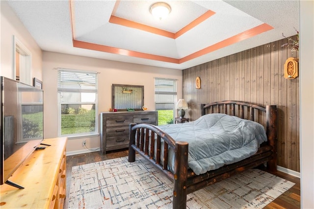 bedroom featuring a tray ceiling, wooden walls, baseboards, and wood finished floors