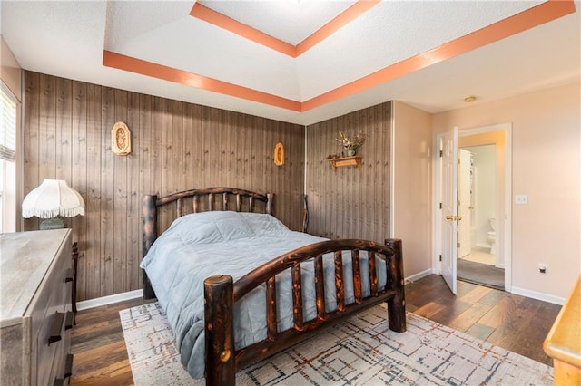 bedroom featuring a raised ceiling, wood walls, baseboards, and wood finished floors