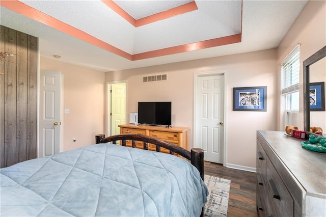 bedroom featuring dark wood-style floors, a raised ceiling, visible vents, and baseboards