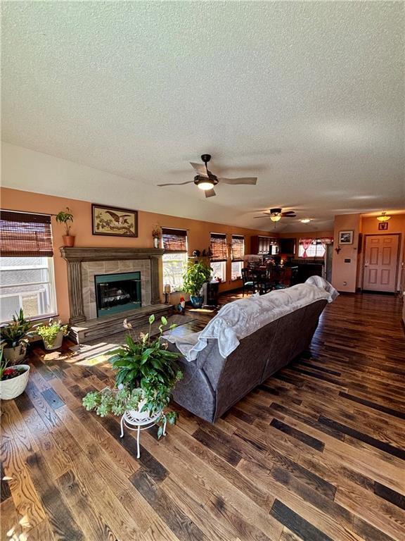 living room featuring a textured ceiling, a tiled fireplace, wood finished floors, and a ceiling fan