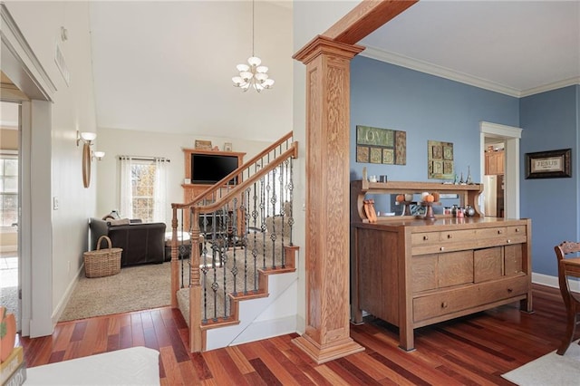 stairway featuring wood-type flooring, ornate columns, crown molding, and a notable chandelier