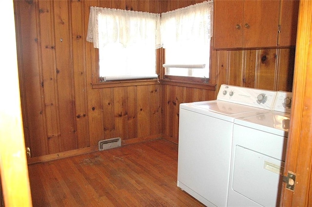 laundry room with hardwood / wood-style floors, wood walls, and washing machine and clothes dryer