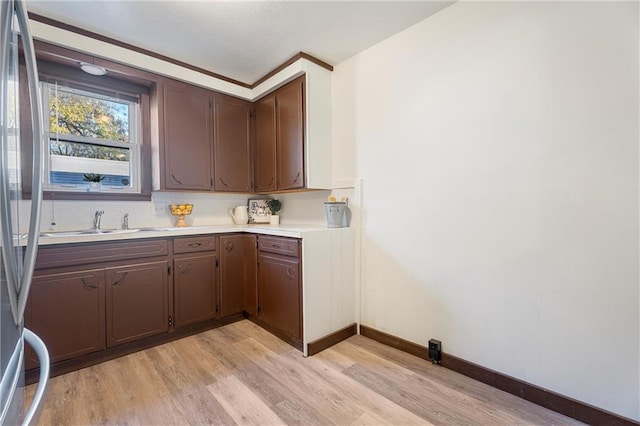 kitchen with stainless steel refrigerator, light hardwood / wood-style flooring, dark brown cabinets, and sink