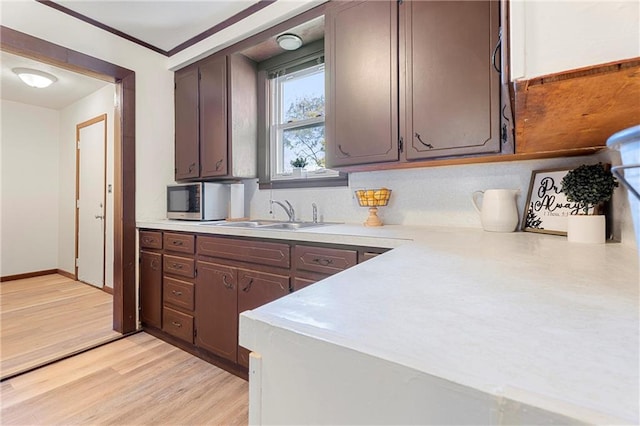 kitchen featuring dark brown cabinets, light hardwood / wood-style floors, ornamental molding, and sink