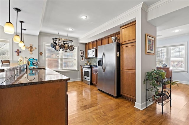 kitchen with sink, decorative light fixtures, light wood-type flooring, ornamental molding, and stainless steel appliances