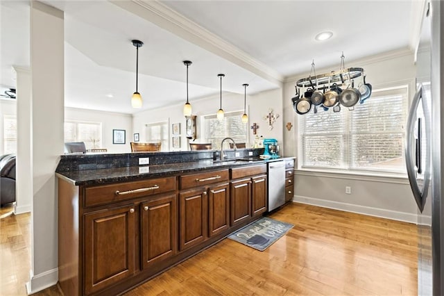 kitchen with dark stone counters, hanging light fixtures, kitchen peninsula, stainless steel appliances, and light hardwood / wood-style flooring