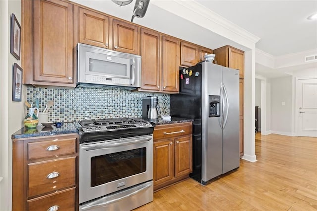 kitchen with appliances with stainless steel finishes, dark stone countertops, backsplash, crown molding, and light wood-type flooring