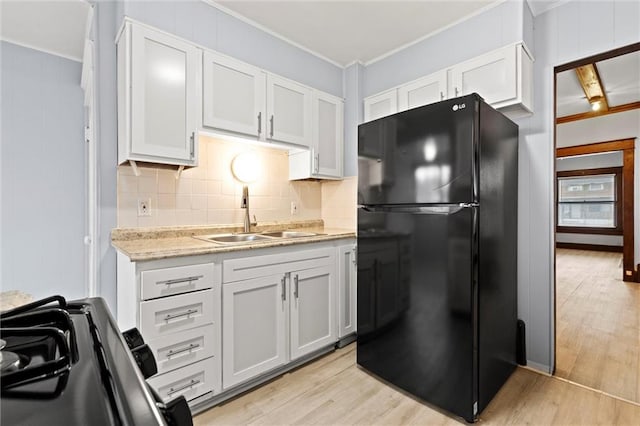 kitchen with black refrigerator, sink, light wood-type flooring, ornamental molding, and white cabinetry